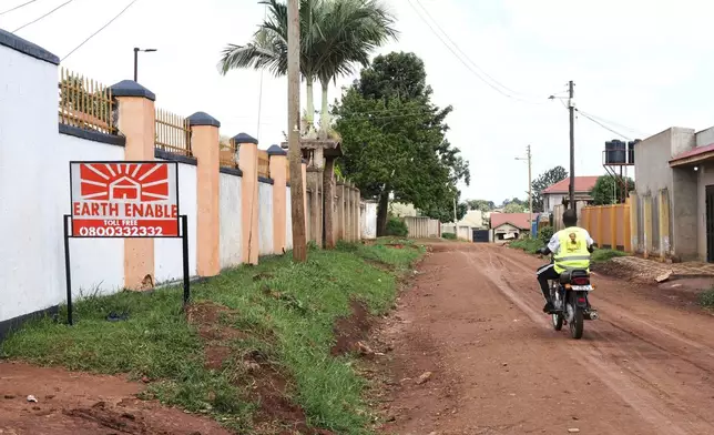 A person rides past a sign for EarthEnable on May 17, 2025, in Jinja, Uganda. (AP Photo/Hajarah Nalwadda)