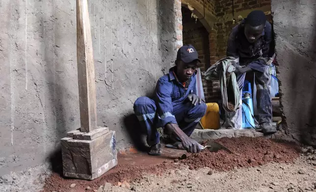 Alex Wanda, left, construction officer of EarthEnable, is helped by his colleague to prepare the ground for a clay-based earthen floor by EarthEnable on May 17, 2025, in Jinja, Uganda. (AP Photo/Hajarah Nalwadda)