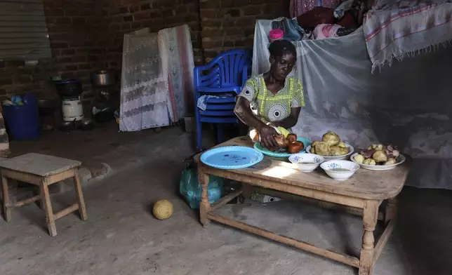 Rehema Namukose prepares a meal inside her home with clay-based earthen floors installed by EarthEnable on May 17, 2025, in Jinja, Uganda. (AP Photo/Hajarah Nalwadda)