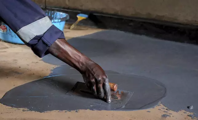 Alex Wanda, a construction officer at EarthEnable, installs paste on floors May 17, 2025, in Jinja, Uganda. (AP Photo/Hajarah Nalwadda)