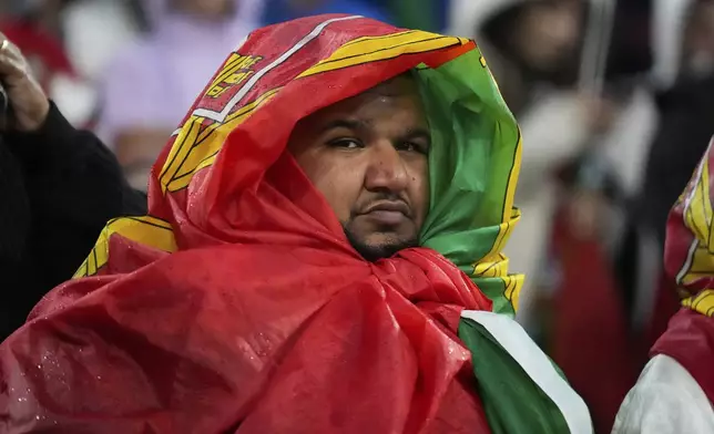 A Portugal fan shields himself from the rain with a flag during a storm before the Nations League semifinal soccer match between Portugal and Germany at the Munich Football Arena, in Munich, Germany, Wednesday, June 4, 2025. (AP Photo/Matthias Schrader)