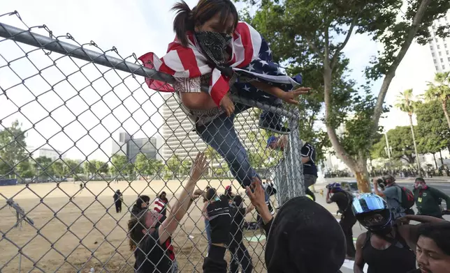 A woman climbs over a fence to escape a police kettle during a protest Saturday, June 14, 2025, in Los Angeles. (AP Photo/Ethan Swope)