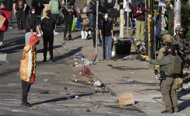 A law enforcement officer points a taser at a person wearing a hot dog costume during a protest Saturday, June 14, 2025, in Portland, Ore. (AP Photo/Jenny Kane)