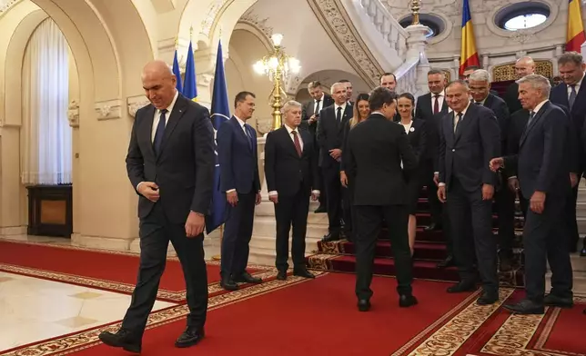 Romanian Prime Minister Ilie Bolojan leaves as Romanian President Nicusor Dan, right, shakes hands with the ministers of the new government after a swearing in ceremony at the Cotroceni Presidential Palace in Bucharest, Romania, Monday, June 23, 2025. (AP Photo/Andreea Alexandru)