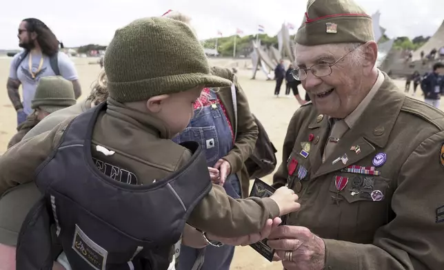World War II veteran Wilbur "Jack" Myers, a 101-year-old who fought in the U.S. Army's 692nd Tank Destroyer Battalion, hands a souvenir postcard of himself to Ryan, a young French boy, on Monday, June 2, 2025, at Omaha beach, which was one of the D-D-day invasion spots on June 6, 1944. (AP Photo/John Leicester)