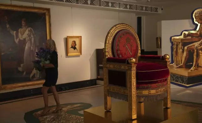 A woman walks past a throne in an exhibition of Napoleon's belongings created by French designer Jean-Charles de Castelbajac at the Sotheby's auction house in Paris Thursday, June 19, 2025 in Paris. (AP Photo/Christophe Ena)