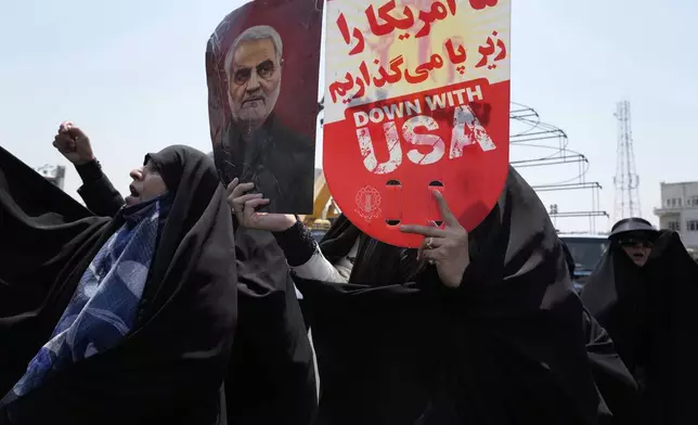 An Iranian protester holds up an anti-U.S. placard and a poster of the late revolutionary guard Gen. Qassem Soleimani, who was killed in a U.S. attack in Iraq in 2020, in an anti-Israeli gathering in Tehran, Iran, Friday, June 13, 2025. (AP Photo/Vahid Salemi)