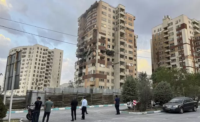 Residents watch a damaged apartment in Tehran, Iran, early Friday, June 13, 2025. Israel attacked Iran's capital early Friday, with explosions booming across Tehran.(AP Photo/Vahid Salemi)