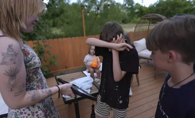 Charlie Lamb, center, who is diagnosed with autism and is non-verbal, uses an AAC device to communicate with a caregiver, Monday, May 12, 2025, in Austin, Texas. (AP Photo/Eric Gay)
