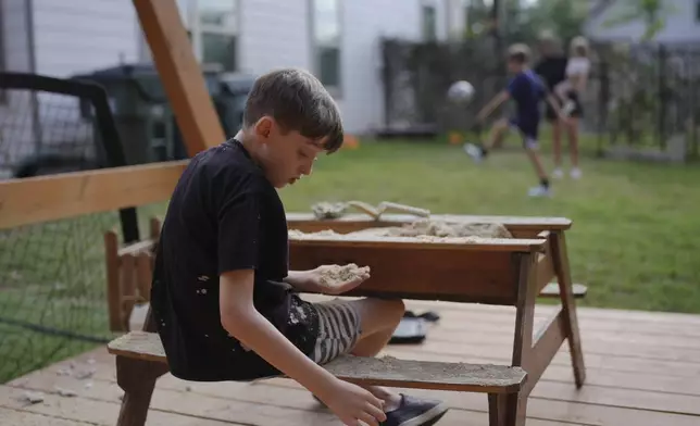 Charlie Lamb, left, who is diagnosed with autism, plays with sand at his home, while his brother Jude and mother Eileen Lamb, who also have autism, and sister Billie, play soccer, Monday, May 12, 2025, in Austin, Texas. (AP Photo/Eric Gay)