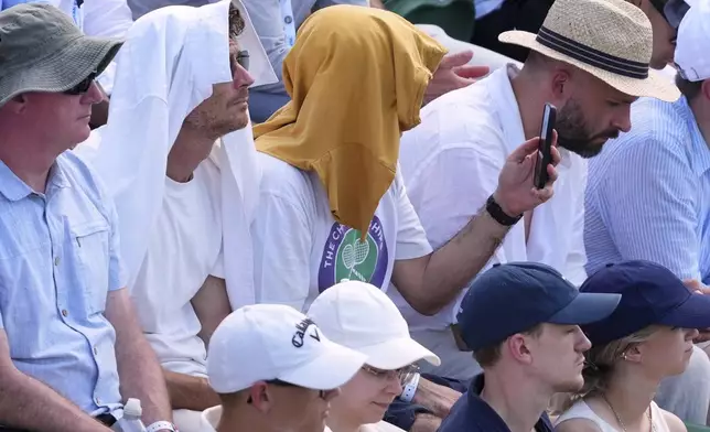 People use towels to protect their head from the sun as they watch a tennis match at the Wimbledon Tennis Championships in London, Monday, June 30, 2025. (AP Photo/Kirsty Wigglesworth)