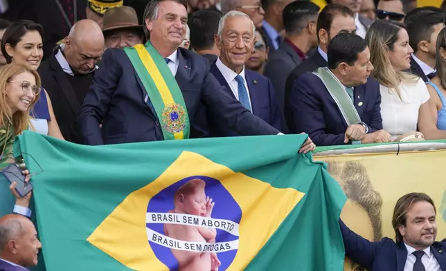 FILE - President Jair Bolsonaro holds onto a Brazilian flag with a message that reads in Portuguese; "Brazil without abortion. Brazil without drugs", during a military parade in Brasilia, Brazil, Sept. 7, 2022. (AP Photo/Eraldo Peres, File)
