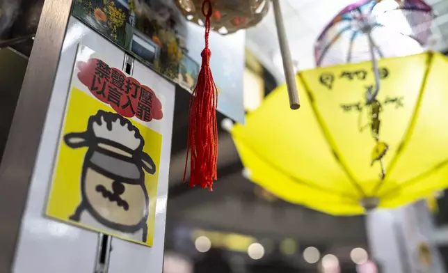 A sticker reads, "Silencing dissent and criminalizing speech," displayed at Chan Kim Kam's stall selling incense and essential oils in Hong Kong, Friday, June 20, 2025. (AP Photo/Chan Long Hei)