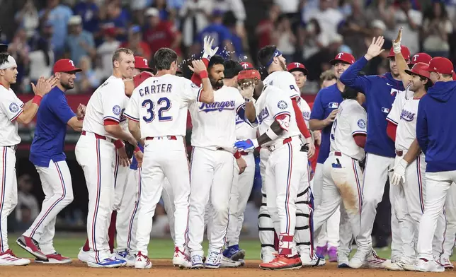 Texas Rangers' Marcus Semien, center with white gloved hand raised, is congratulated by teammates after driving in the winning run in the 10th inning of a baseball game against the Seattle Mariners, Saturday, June 28, 2025, in Arlington, Texas. (AP Photo/Tony Gutierrez)