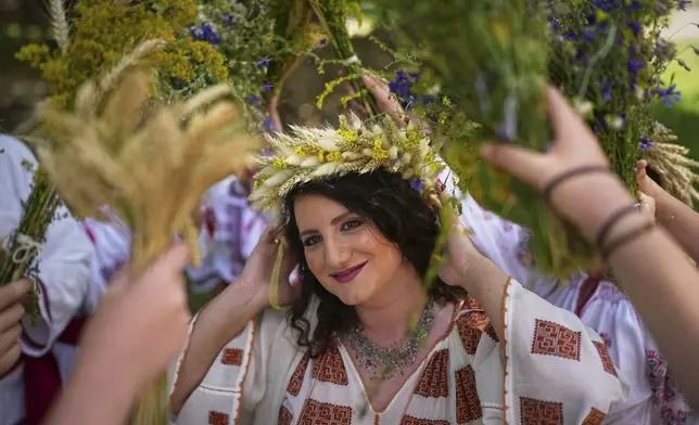 Women, wearing crowns made of flowers, dance during an event inspired by pre-Christian traditions, in which fairies, called in Romanian "Sanziene," come to earth around the summer solstice bringing fertility to land and beings, at the Dimitrie Gusti Village Museum in Bucharest, Romania, Tuesday, June 24, 2025. (AP Photo/Andreea Alexandru)