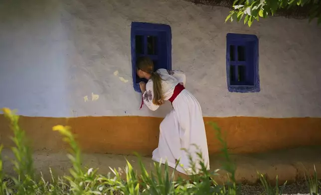 Alisa, 9 years-old, looks inside a village home, during an event inspired by pre-Christian traditions, in which fairies, called in Romanian "Sanziene," come to earth around the summer solstice bringing fertility to land and beings, at the Dimitrie Gusti Village Museum in Bucharest, Romania, Tuesday, June 24, 2025. (AP Photo/Andreea Alexandru)