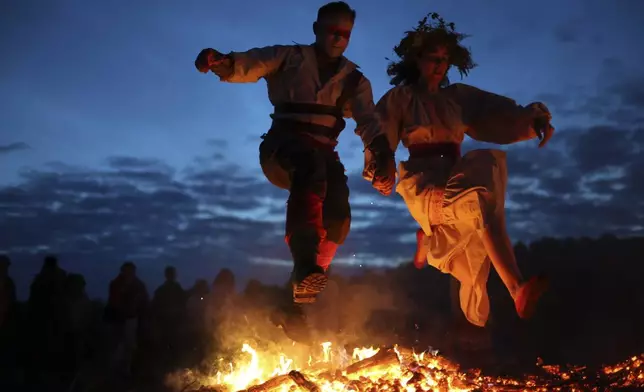 People wearing traditional Russian village-style clothes celebrate the summer solstice near a bonfire in the village of Okunevo, about 200 kilometers (125 miles) northeast of the Siberian city of Omsk, Russia, in Okunevo, Russia, Sunday, June 22, 2025. (AP Photo/Evgeniy Sofiychuk)
