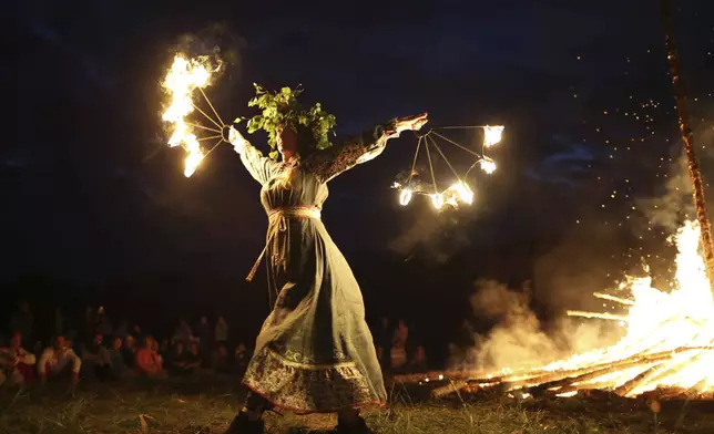 People wearing traditional Russian village-style clothes celebrate the summer solstice near a bonfire in the village of Okunevo, about 200 kilometers (125 miles) northeast of the Siberian city of Omsk, in Okunevo, Russia, Sunday, June 22, 2025. (AP Photo/Evgeniy Sofiychuk)