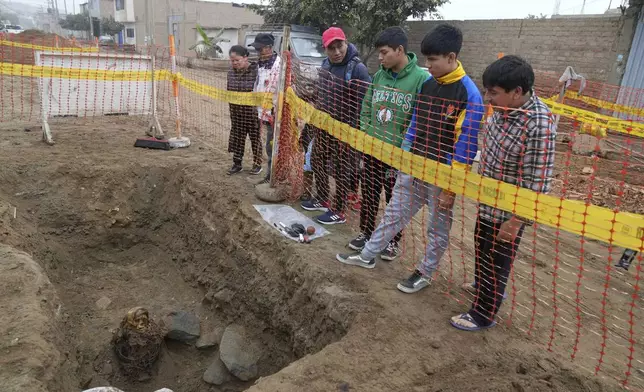 Locals look at an ancient mummy which archeologists identify as female and from the pre-Inca Chancay culture during its excavation after being discovered by city workers digging a natural gas line for the company Calidda in the district of Puente Piedra on the outskirts of Lima, Peru, Wednesday, June 18, 2025. (AP Photo/Martin Mejia)