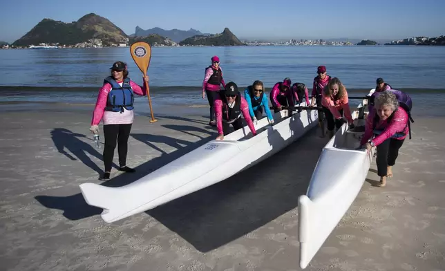 The Rosas Va'a Hawaiian canoeing team, whose members are women who have undergone cancer treatment, push their canoes out of the water on to Charitas Beach after training in Niteroi, Rio de Janeiro state, Thursday, June 26, 2025. At right is the team's trainer Leticia Mendez. (AP Photo/Bruna Prado)
