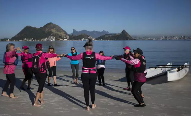 The Rosas Va'a Hawaiian canoeing team, whose members are women who have undergone cancer treatment, gather after training on the water, at Charitas Beach in Niteroi, Rio de Janeiro state, Thursday, June 26, 2025. (AP Photo/Bruna Prado)