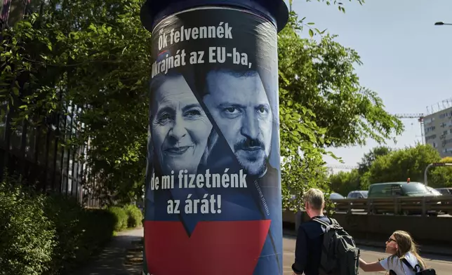People pass by a Hungarian government billboard, opposing Ukraine's EU membership, showing European Commission President Ursula von der Leyen and Ukrainian President Volodymyr Zelenskyy, which reads "They would bring Ukraine into the EU, but we would pay the price! Let's vote no!", In Budapest, Hungary, Wednesday, June 11, 2025. (AP Photo/Bela Szandelszky)