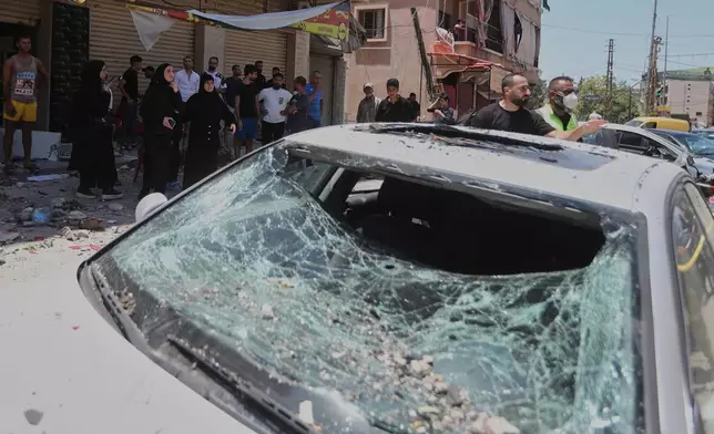 People gather next to a car that was damaged in an Israeli airstrike in Nabatieh town, south Lebanon, Friday, June 27, 2025. (AP Photo/Mohammed Zaatari)