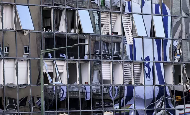 The Israeli flag is reflected in the windows of a damaged building in Ramat Gan, Israel, two days after it was hit by a missile launched from Iran, Saturday, June 21, 2025. (AP Photo/Ohad Zwigenberg)