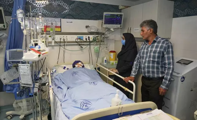 Parnia Rahmanian, 13, lies unconscious in a hospital bed following Israeli strike that targeted her neighborhood, as a nurse, second right, and a relative look on, in Tehran, Iran, Saturday, June 21, 2025. (AP Photo/Vahid Salemi)