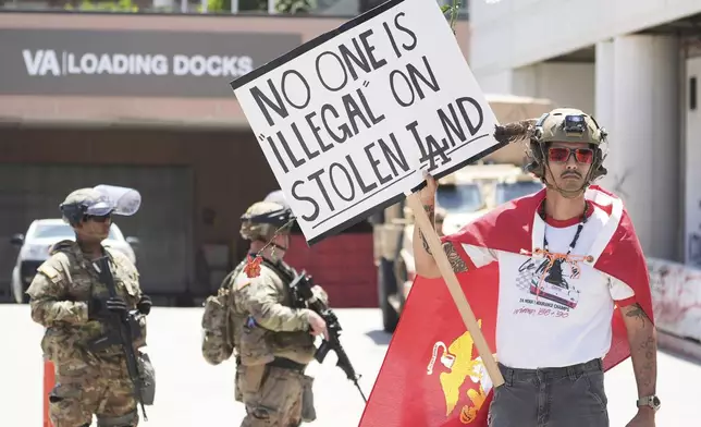 Jack Murillo, a Marine veteran, holds a sign in front of law enforcement guarding a federal building on Tuesday, June 17, 2025, in Los Angeles. (AP Photo/Damian Dovarganes)