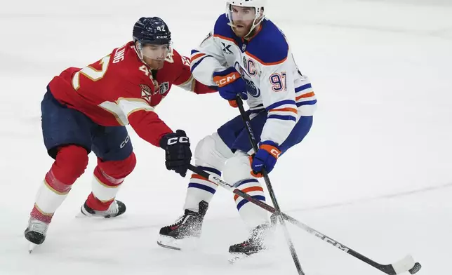 Florida Panthers' Gustav Forsling (42) pokes the puck away from Edmonton Oilers' Connor McDavid (97) during the second period in Game 3 of the NHL hockey Stanley Cup finals in Sunrise, Fla., Monday, June 9, 2025. (Nathan Denette/The Canadian Press via AP)