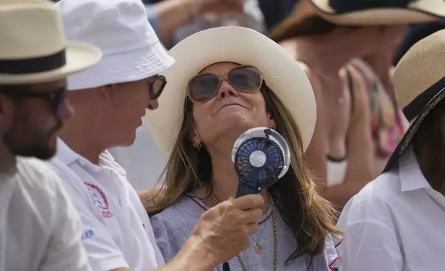 A spectator uses fan to keep cool in the stands during the match of the Queen's Club Championships tennis tournament in London, Friday, June 20, 2025. (AP Photo/Kin Cheung)