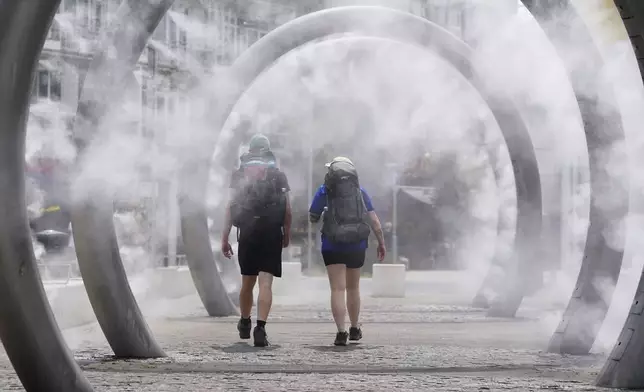 Walkers cool off as they walk through a water feature spraying a fine mist in Dover, England, Friday, June 20, 2025. (Gareth Fuller/PA via AP)