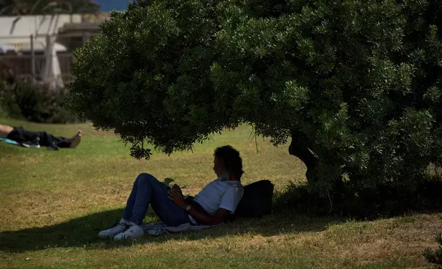 A man writes in the shade of a tree during high temperatures in Barcelona, Spain, Friday, June 20, 2025. (AP Photo/Emilio Morenatti)