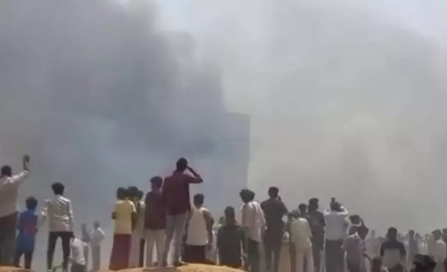 People watch smoke rising after an airplane crashed in Ahmedabad, Gujarat state, India, Thursday, June 12, 2025. (Mohan Nakum via AP)