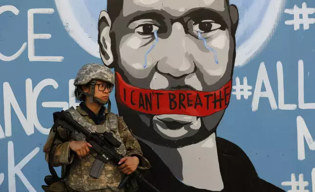 FILE — In this June 4, 2020 file photo a member of the California National Guard stands in front of a mural depicting George Floyd in Los Angeles. On Thursday June 11, 2020, California Gov. Gavin Newsom's Administration announced it cost more than $24 million to deploy 8,000 National Guard members for 18 days during the recent protests of racial injustice inspired by the death of Floyd on May 25 in Minneapolis. (AP Photo/Jae C. Hong, File)