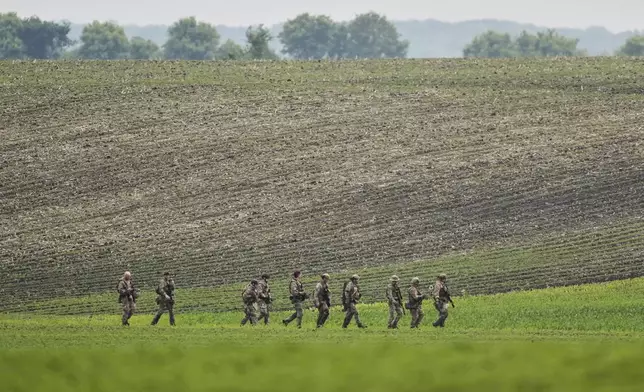 Members of law enforcement agencies walk through a field near a vehicle suspected to belong to shooting suspect, Vance Boelter, Sunday, June 15, 2025, in Belle Plaine, Minn. (AP Photo/George Walker IV)