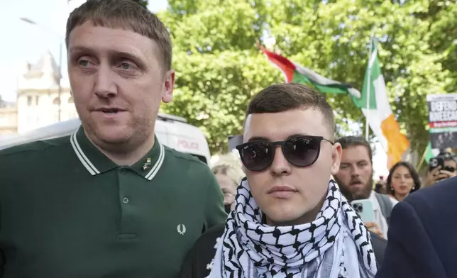 Liam Óg Ó hAnnaidh, aka Mo Chara, right, a member of the Irish language band Kneecap, leaves Westminster Magistrates Court London, Wednesday, June 18, 2025, where he is charged with a terrorism offence relating to displaying a flag in support of Hezbollah during a performance with the band in November 2024. (AP Photo/Kin Cheung)