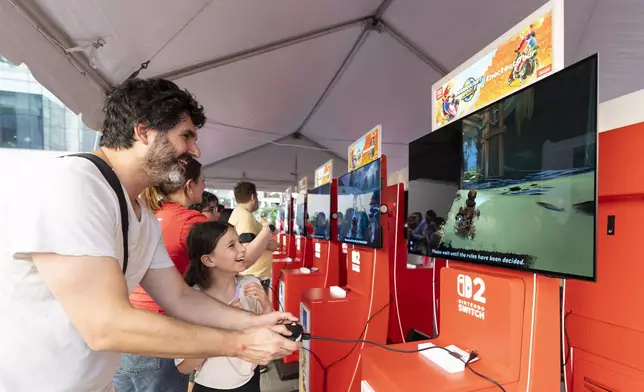 In this photo provided by Nintendo of America, Trenton B. and Abigail B. play the Mario Kart World game in Rockefeller Plaza ahead of purchasing their Nintendo Switch 2 system at the Nintendo NEW YORK store. Nintendo Switch 2, the seamlessly social, all-in-one Nintendo platform, is available now.