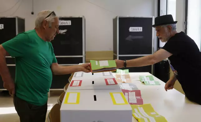 Ballot papers are handed over to a citizen, left, to vote on referendums on citizenship and job protections, at a polling station in Rome, Sunday, June 8, 2025. (Cecilia Fabiano/LaPresse via AP)