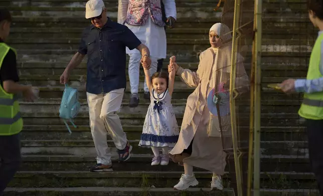 People hold a little girl above the ground as they come down stairs to attend Eid al-Adha prayers at the Dinamo stadium in Bucharest, Romania, Friday, June 6, 2025. (AP Photo/Vadim Ghirda)