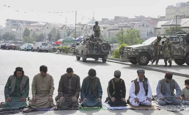 Afghan Muslims perform Eid al-Adha prayer while Taliban fighters stand guard outside the Shah-Do Shamshira Mosque in Kabul, Afghanistan, Saturday, June 7, 2025. (AP Photo/Ebrahim Noroozi)