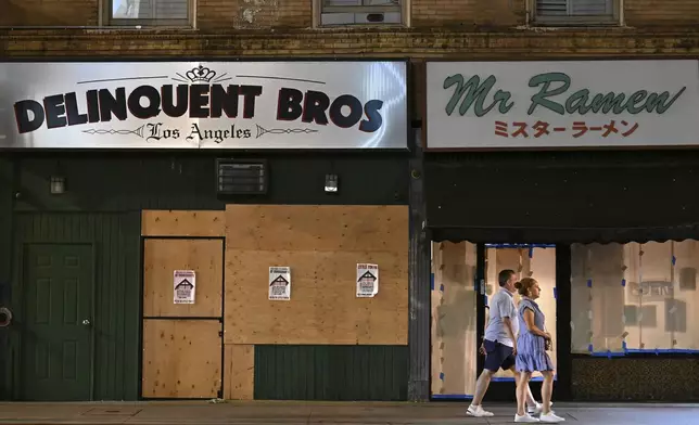 A couple walks past boarded up businesses along 1st St. in Little Tokyo Tuesday, June 17, 2025, in Los Angeles. (AP Photo/Wally Skalij)
