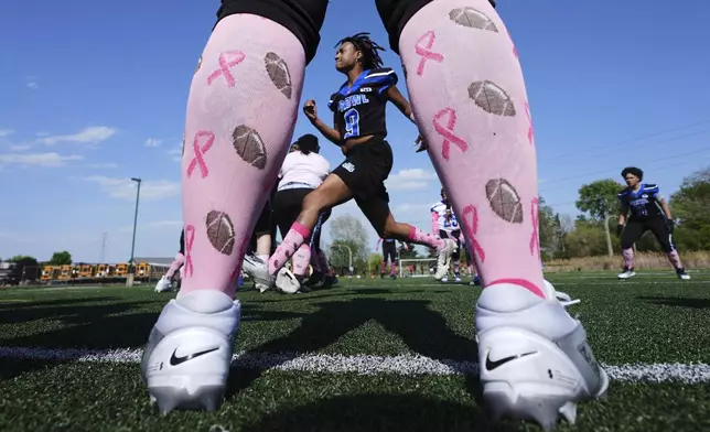 Detroit Prowl's Danyelle Kerse, framed by a teammate wearing football breast cancer knee high socks, warms up before an AWFL women's football game against the Lansing Legacy, in Allen Park, Mich., Saturday, May 10, 2025. (AP Photo/Paul Sancya)