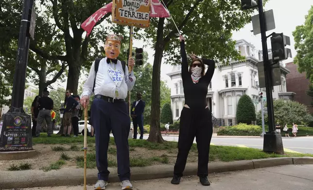 A demonstrator with a flag and another wearing a President Donald Trump mask carrying a sign participate in a protest taking place on the day of a military parade commemorating the Army's 250th anniversary, coinciding with Trump's 79th birthday, Saturday, June 14, 2025, in Washington. (AP Photo/Evan Vucci)