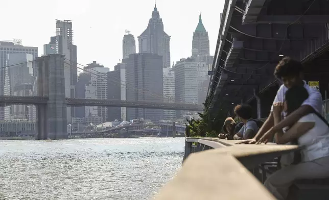 A view of lower Manhattan and the Brooklyn Bridge is seen as people sit along the East River, during an air quality alert issued for the New York region due to wildfire smoke from Canada, Wednesday, June 4, 2025, in New York. (AP Photo/Heather Khalifa)