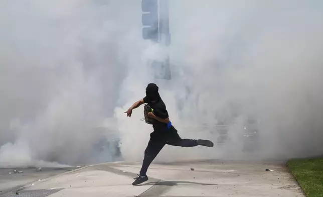 A protester throws a rock amidst tear gas from law enforcement during a demonstration after federal immigration authorities conducted operations, Saturday, June 7, 2025, in the Paramount section of Los Angeles. (AP Photo/Eric Thayer)