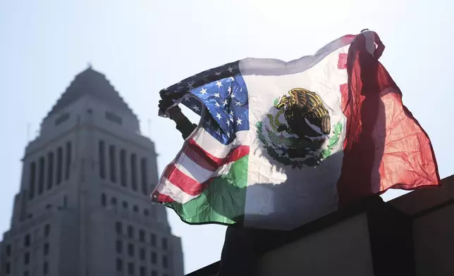 A person holds up an American and Mexican flag outside the Federal Building after federal immigration authorities conducted an operation Friday, June 6, 2025, in Los Angeles. (AP Photo/Damian Dovarganes)
