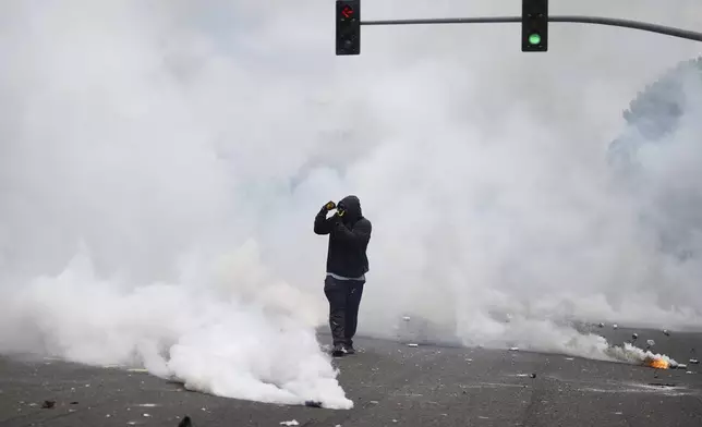 A protester gestures amidst tear gas from law enforcement during a protest in the Paramount section of Los Angeles, Saturday, June 7, 2025, after federal immigration authorities conducted operations. (AP Photo/Eric Thayer)