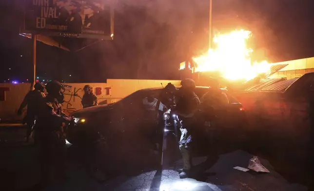 Law enforcement help a person out of a car as a fire burns during a protest in Compton, Calif., Saturday, June 7, 2025, after federal immigration authorities conducted operations. (AP Photo/Ethan Swope)
